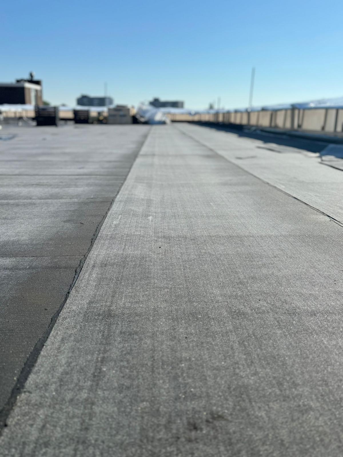 Plat dak met nieuwe bitumen dakbedekking onder heldere lucht, uitgevoerd door Uw Aannemers – dakdekker in Rotterdam.